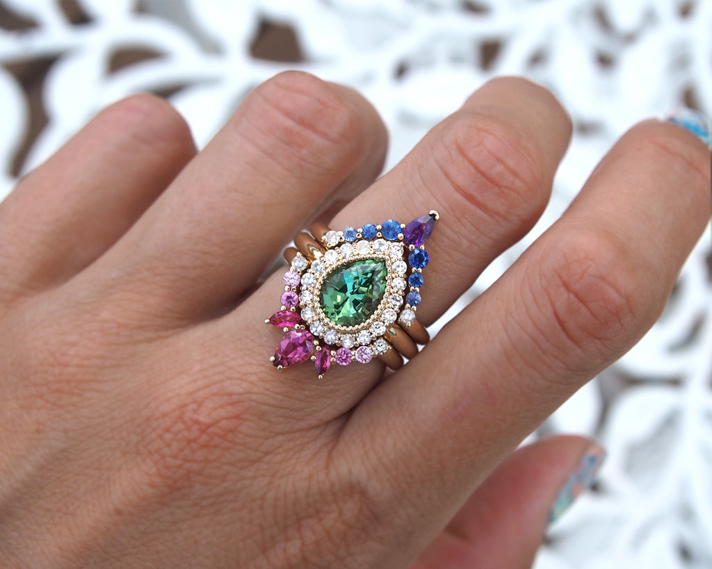 Non solitaire engagement ring featuring a Peacock Forest Flower design with green tourmaline, diamonds, and sapphires.