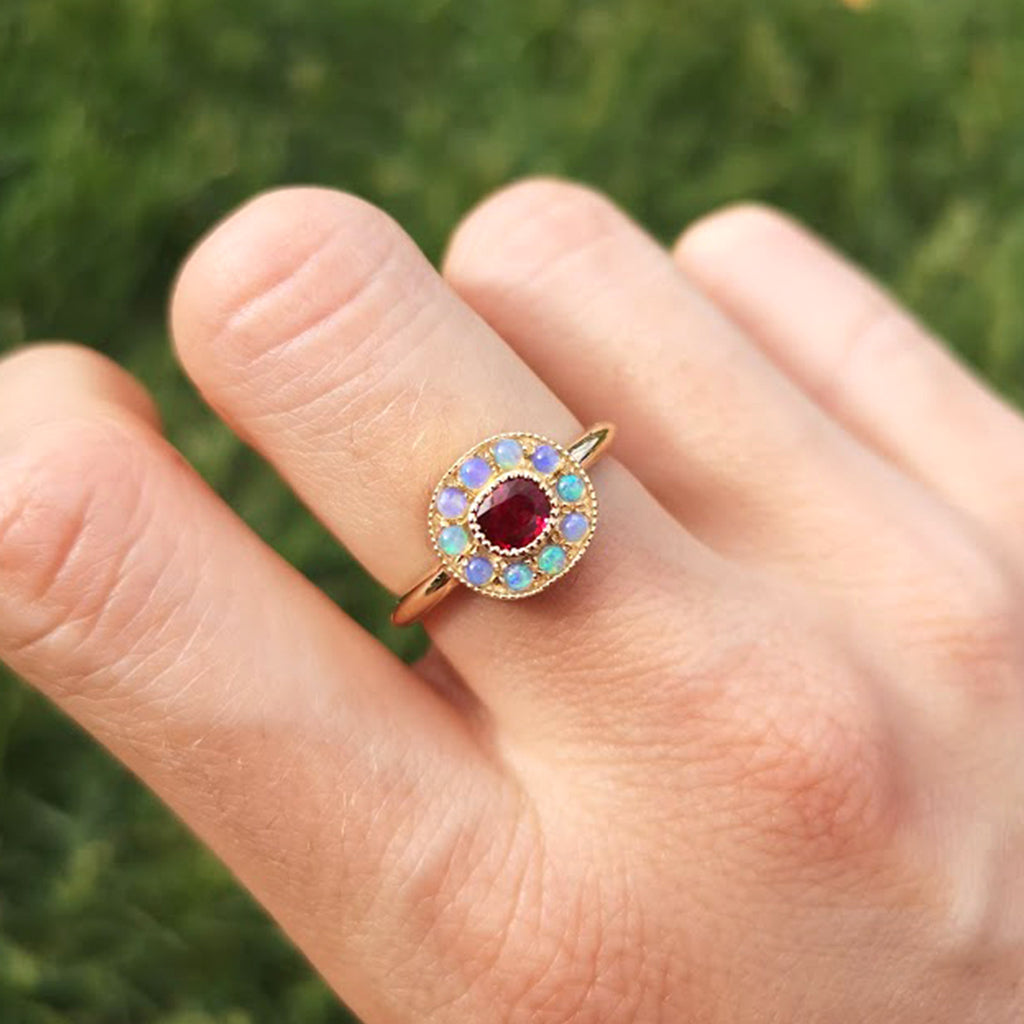 Close-up view of the one-of-a-kind Ruby halo ring with mini Australian opals, retro-antique inspired design by Lico Jewelry, set in solid 14k yellow gold, on a woman's finger.