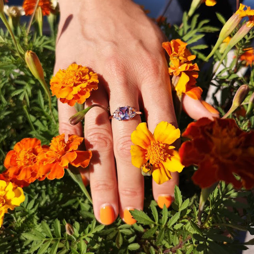 Woman's hand with Lilac Roots ring on the engagement finger, lying in a flower bed with beautiful colors. Custom orders available.