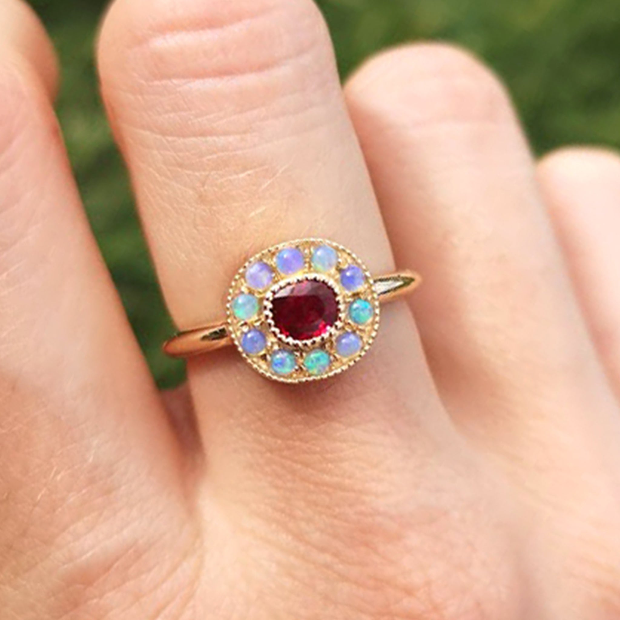 Close-up view of the one-of-a-kind Ruby halo ring with mini Australian opals, retro-antique inspired design by Lico Jewelry, set in solid 14k yellow gold, on a woman's middle finger.