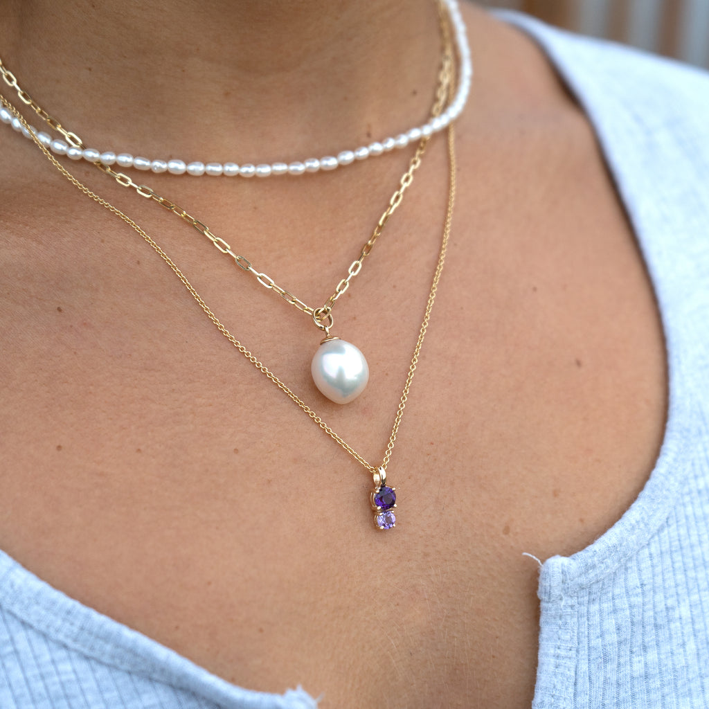 A woman wearing a beautiful Aquarius pendant in 14K yellow gold from Lico Jewelry, paired with a pearl necklace