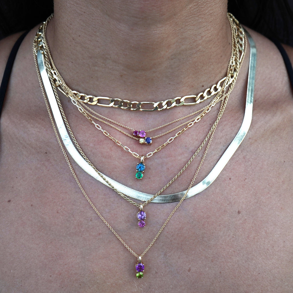 Woman's neck adorned with several other Lico Jewelry necklaces layered and styled, featuring the 2 stone pendant in solid 14k yellow gold with genuine London blue topaz and emerald on a 20-inch rolo chain. Handcrafted by Lico Jewelry in Montreal.