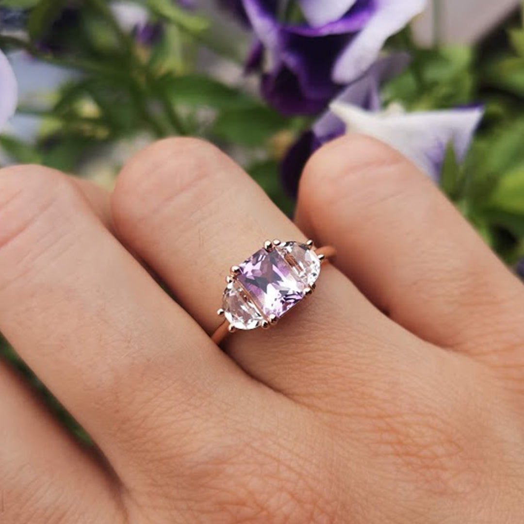 Woman's hand with Lilac Roots ring on the engagement finger, bending the fingers with flowers in the background. Order yours now.