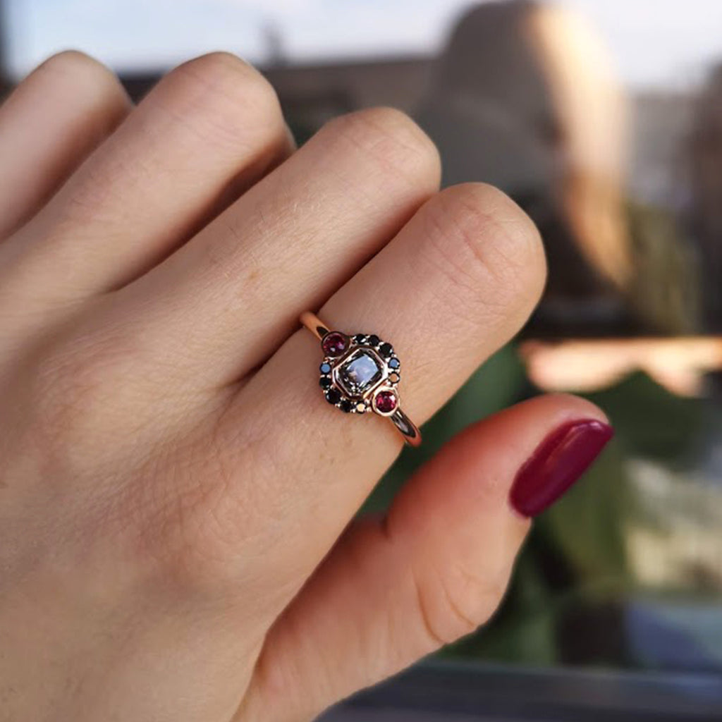 La Couche du Diable ring from Lico Jewelry in Montreal, featuring a unique salt and pepper diamond surrounded by black diamonds and rubies set in 18k rose gold on a pointer finger as the fingers bend
