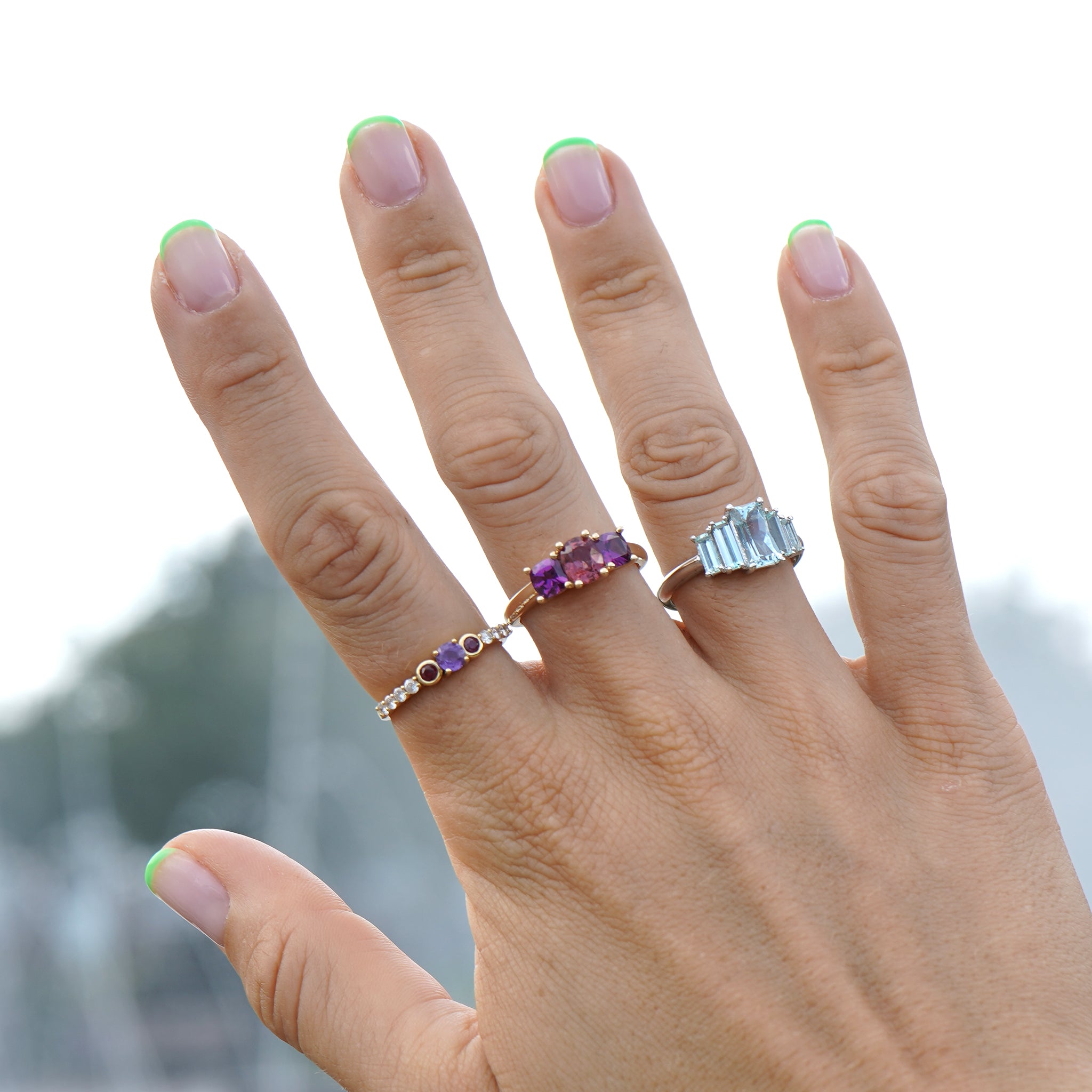 Woman's hand pointing up to the sky showing off three Lico Jewelry rings on middle fingers, including Marine Deco Ring with aquamarine gemstones in platinum.