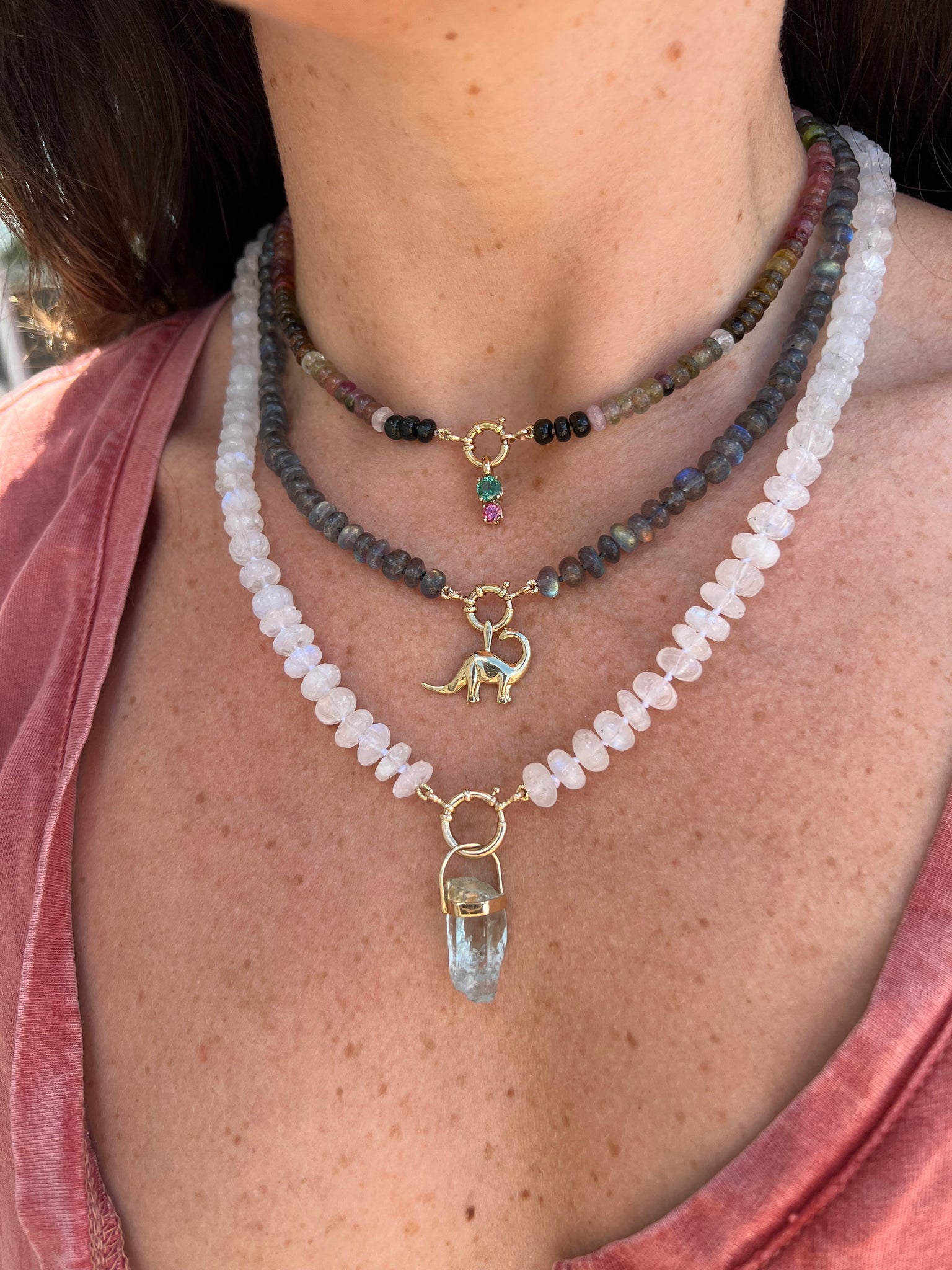 Model wearing the Spring mix 2 pendant by Lico Jewelry layered with other necklaces and pendants. She is wearing a light pink shirt and the pendant features genuine green and pink tourmaline stones in 14k yellow gold on a rolo chain
