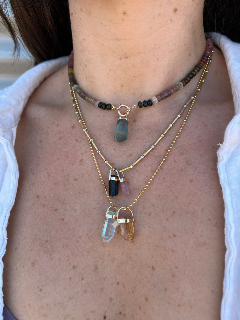 A woman wearing a beautiful Aquamarine crystal pendant in 14K yellow gold from Lico Jewelry, highlighting the vibrant blue color of the Aquamarine