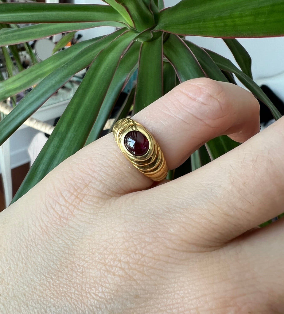 Hand model wearing the vintage 18K cabochon garnet ring on the pinky finger, with a lush green plant in the background close up beautiful