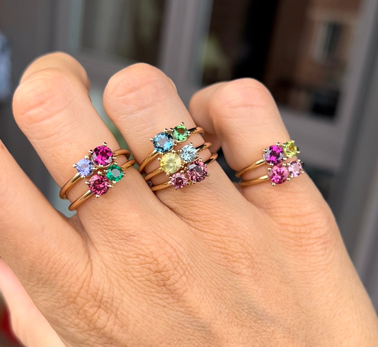 A woman's hand with multiple 2 stone rings by Lico Jewelry on three fingers, showcasing different combinations.