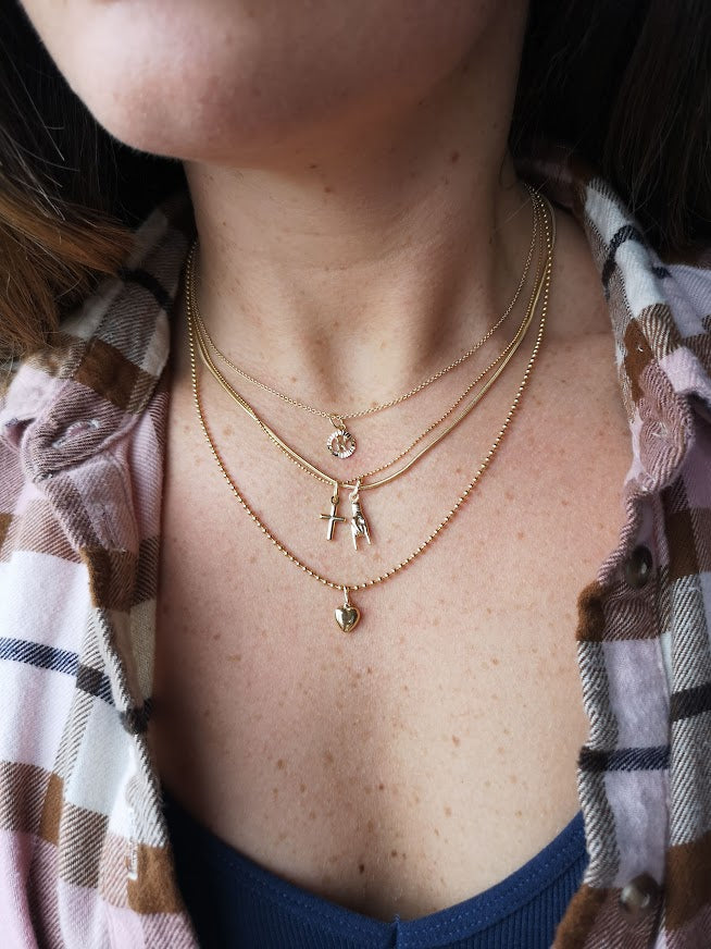 Multiple Lico Jewelry necklaces layered on a woman's neck, including the Mano cornuto charm necklace from Montreal, on a plaid shirt