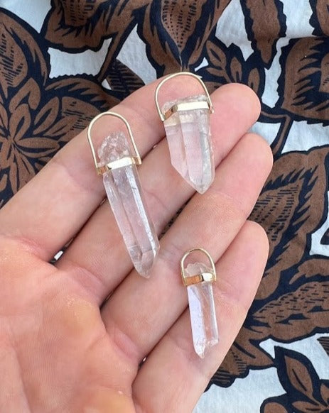 Lico Jewelry Clear Quartz Crystal Pendants, set in 14K yellow gold, on a woman's hand. Montreal-based company.