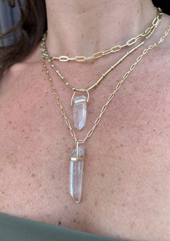 woman wearing a clear quartz crystal pendant from Lico Jewelry, a Montreal-based company, paired with other beautiful necklaces.