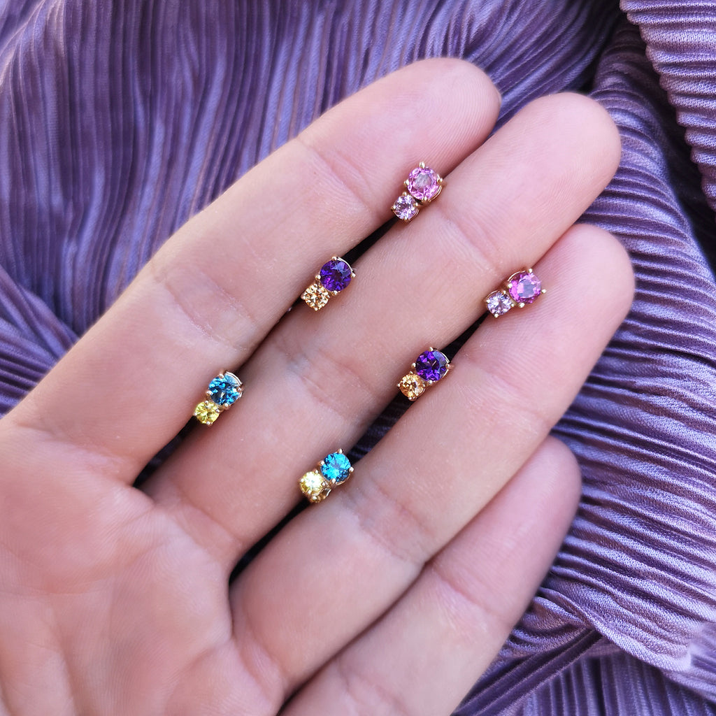 Three sets of Lico Jewelry earrings, including Mariner Earrings with Swiss Blue Topaz and Yellow Sapphire, on a woman's palm with a purple background.