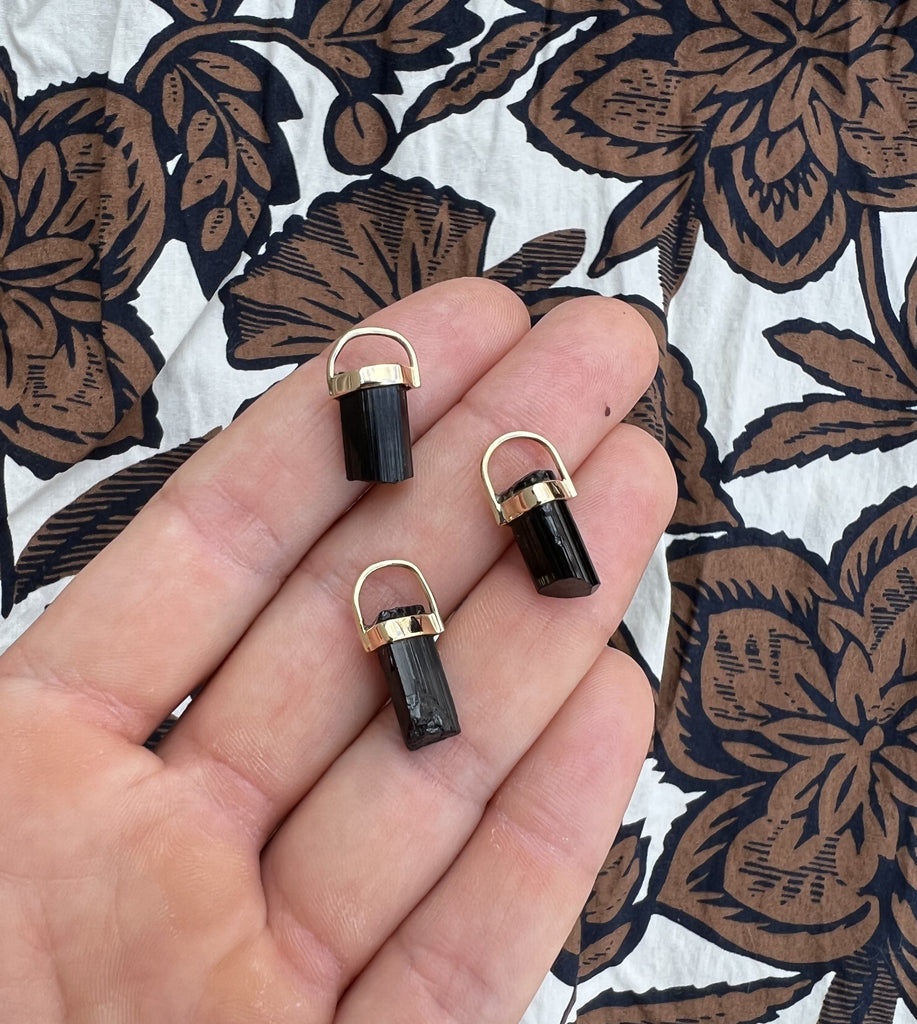 3 black tourmaline rough crystal pendants from Lico Jewelry in a woman's hand" "Multiple black tourmaline rough crystal pendants from Lico Jewelry on a woman's hand