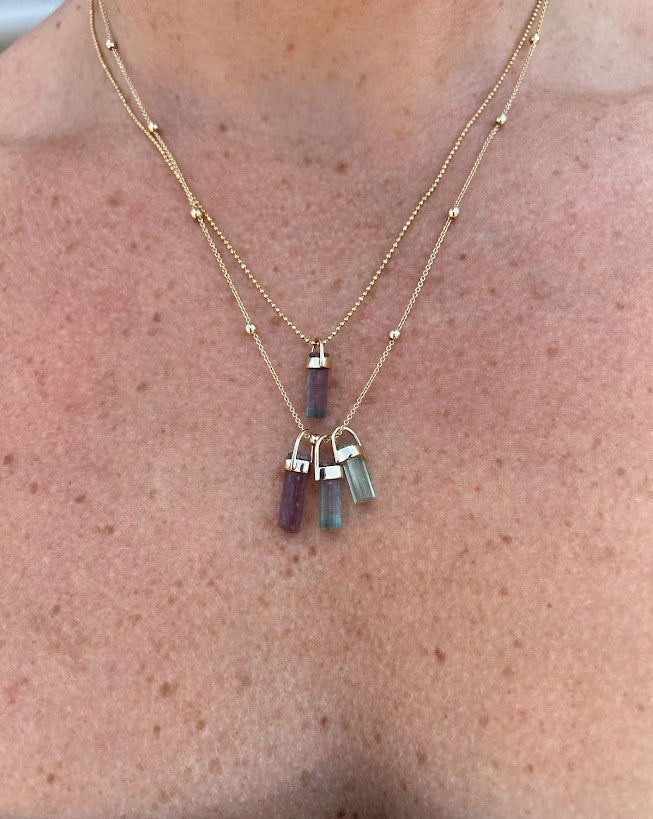 Woman wearing two necklaces, one with one tourmaline crystal pendant and one with three pendants, Lico Jewelry