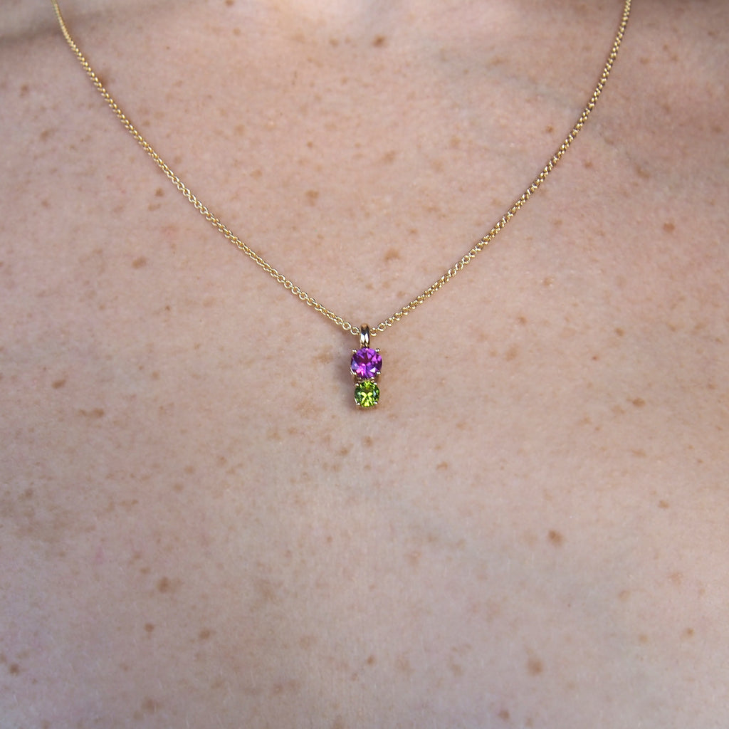 Image of woman's neck with necklace on thin chain: Rhododendron pendant with rhodolite garnet and peridot stones on a thin chain in solid 14k yellow gold