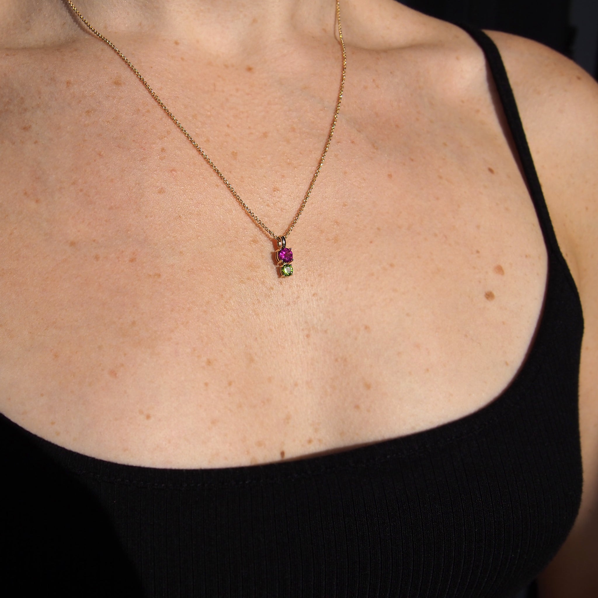 Image of woman wearing necklace with black tank top: Woman wearing Rhododendron pendant with rhodolite garnet and peridot stones on a 20-inch rolo chain in solid 14k yellow gold